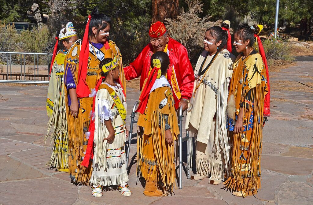 An elder with youth dressed in traditional tribal garments during the Native American Heritage Month celebrations at Grand Canyon National Park